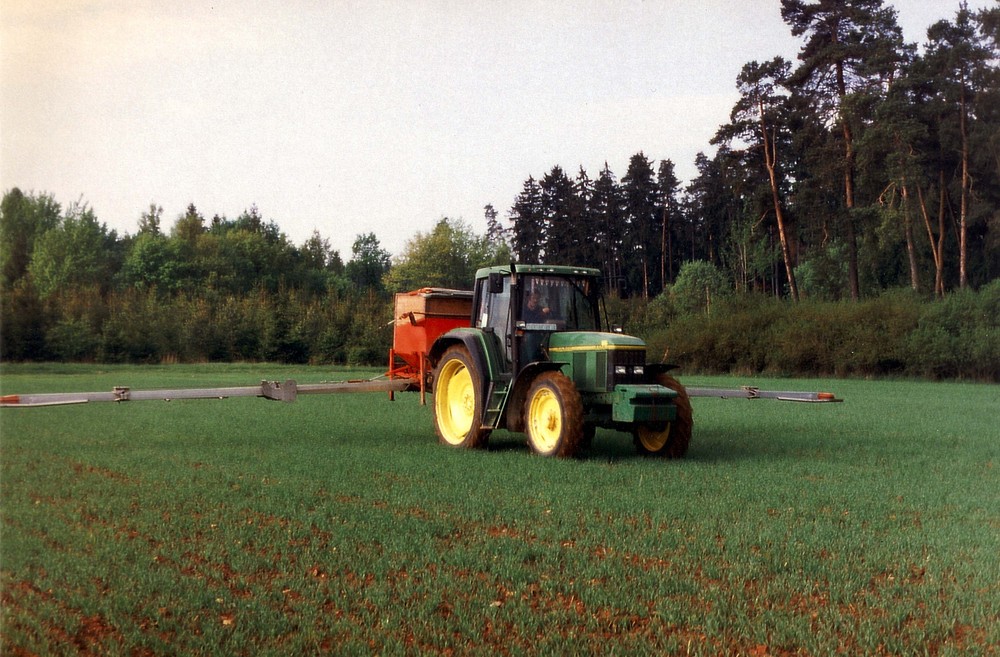 Traktor mit Anbaudüngerstreuer auf Getreidefeld