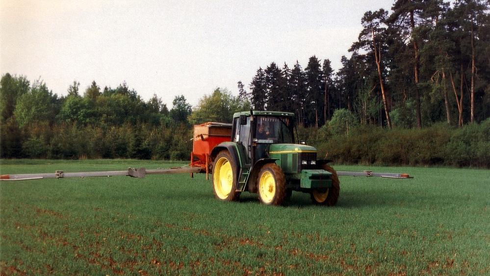 Traktor mit Anbaudüngerstreuer auf Getreidefeld