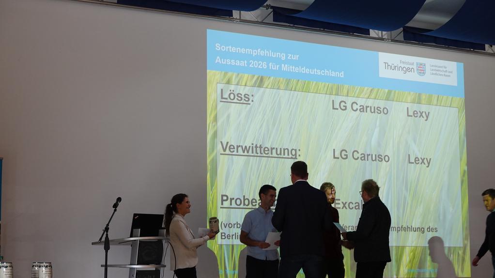 Mehrere Personen stehen vor einer großen Leinwand mit Text zur Sortenempfehlung für Aussaat 2026 in Mitteldeutschland, darunter die Sorten LG Caruso und Lexy.
