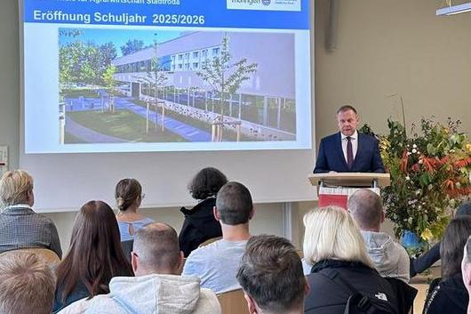 Vortragender in Anzug an Rednerpult vor Publikum, Projektion mit Text 'Friedrich Gottlob Schulze Fachschule für Agrarwirtschaft Stadtroda Eröffnung Schuljahr 2025/2026' und Foto eines Schulgebäudes.