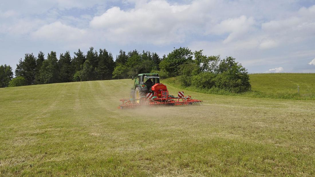 Traktor mit rot lackiertem Anbaugerät fährt über grasbewachsenen Hügel unter bewölktem Himmel.