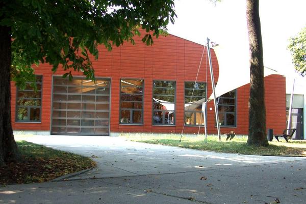 Gebäude mit roter Fassade und großen Fenstern, davor gepflasterter Weg und Bäume.