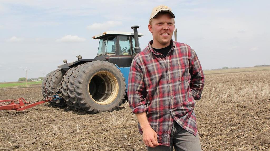 Mann in Arbeitskleidung vor einem Traktor auf dem Feld