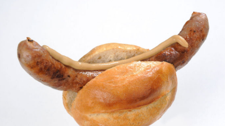 Eine Thüringer Rostbratwurst in hellem Brötchen mit gelbem Senf vor weißem Hintergrund