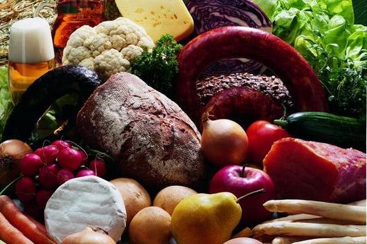 Eine Vielzahl von Lebensmitteln, darunter Gemüse, Obst, Käse, Brot, Eier und Getränke, angeordnet auf einer grünen Oberfläche.
