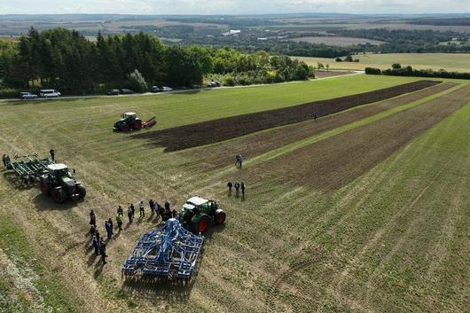 Luftaufnahme von einem Feld mit mehreren Traktoren und einer Gruppe Menschen, die auf dem Acker stehen.