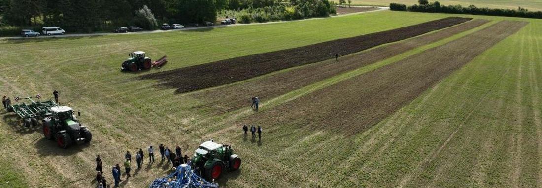 Luftaufnahme von einem Feld mit mehreren Traktoren und einer Gruppe Menschen, die auf dem Acker stehen.