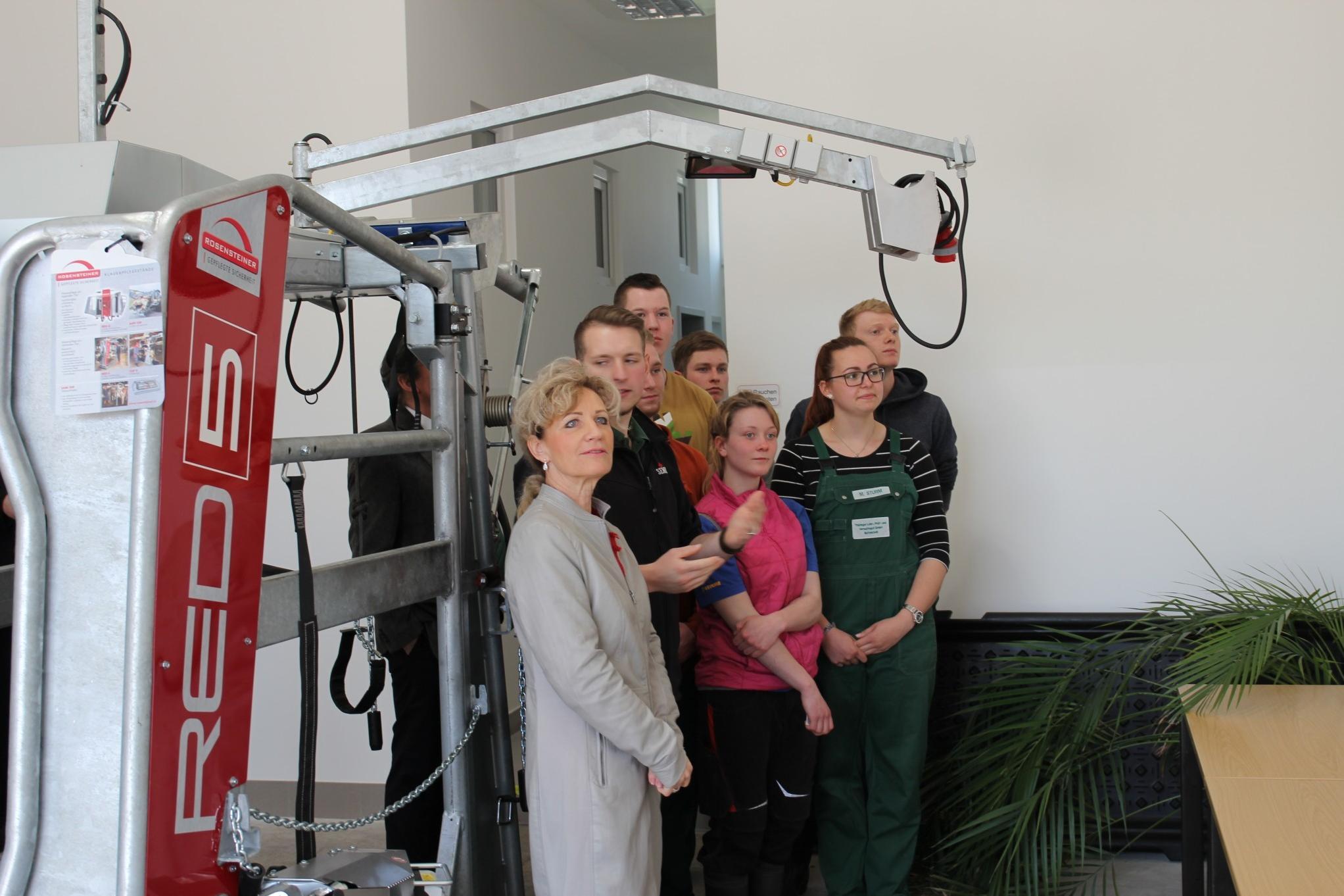 Gruppe von Personen steht neben einer großen, weißen Maschine mit rotem Schriftzug 'RED 5' in einem Raum mit weißen Wänden und grünen Pflanzen.