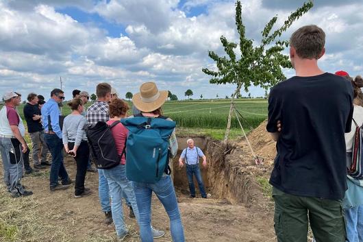 Landwirt Dr. E. Zschoche zeigt das Wachstum der Baumwurzeln an einem Bodenprofil