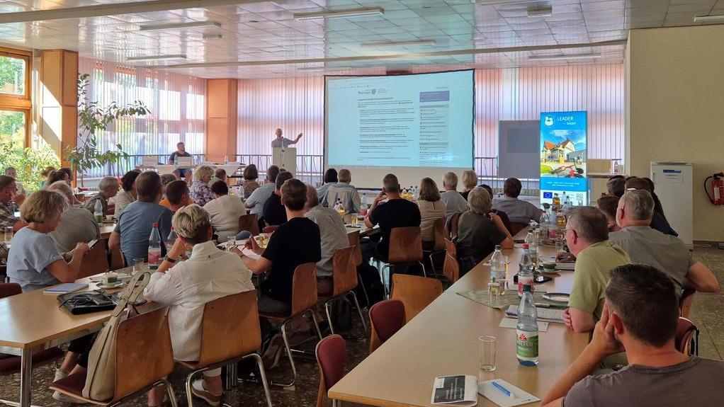 Viele Menschen sitzen in einem Raum und hören sich einen Vortrag an.