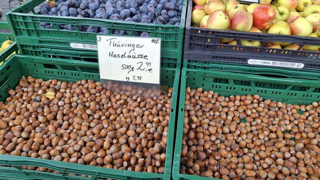 Grüne Kisten mit Haselnüssen, Äpfeln und Pflaumen auf Marktstand, Preisschilder mit handgeschriebener Beschriftung
