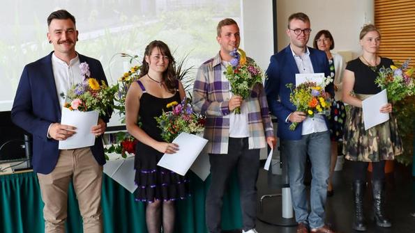 Mehrere Personen stehen nebeneinander, halten Urkunden und bunte Blumensträuße, im Hintergrund Projektion mit Text 'Fachschule Gartenbau 18.07.2025'.