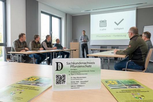 Personen sitzen in einem Seminarraum an Tischen, während eine Person vor einer Leinwand mit der Aufschrift '3 Jahre Gültigkeit' und 'Pflanzenschutz - Fortbildung' steht.