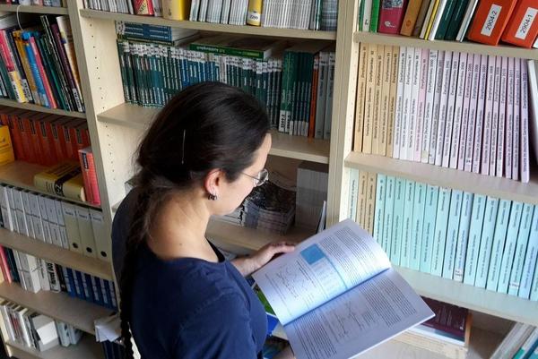Frau vor Bücherregal blättert Berichte durch