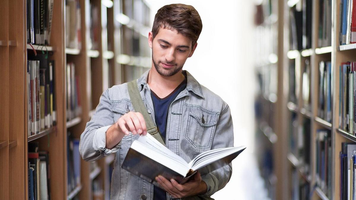 Student mit Buch in der Hand zwischen Bücherregalen